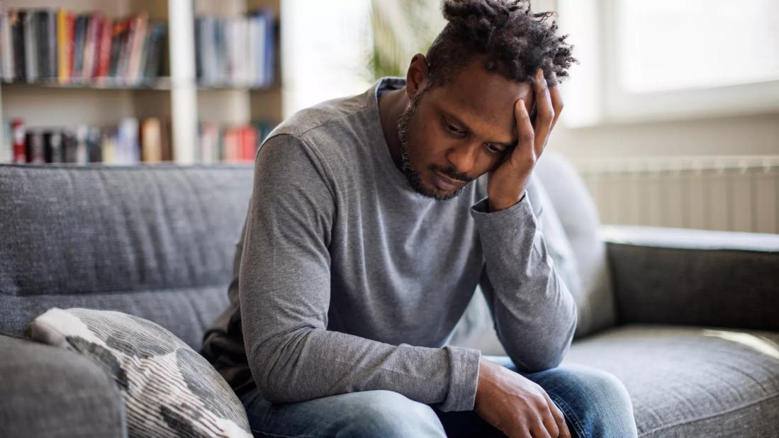 Male sitting on couch with head in hand, looking forlorn