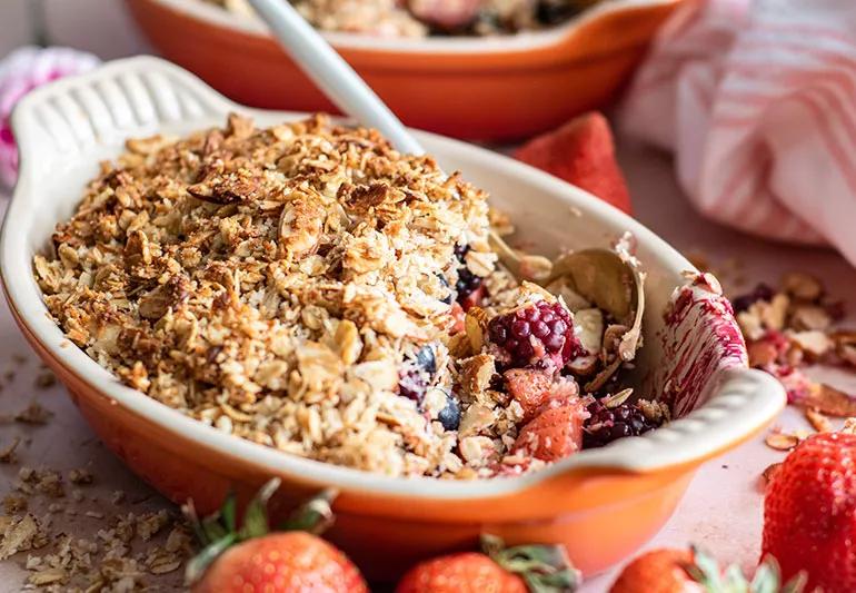 Warm berry crisp in a bowl with strawberries nearby