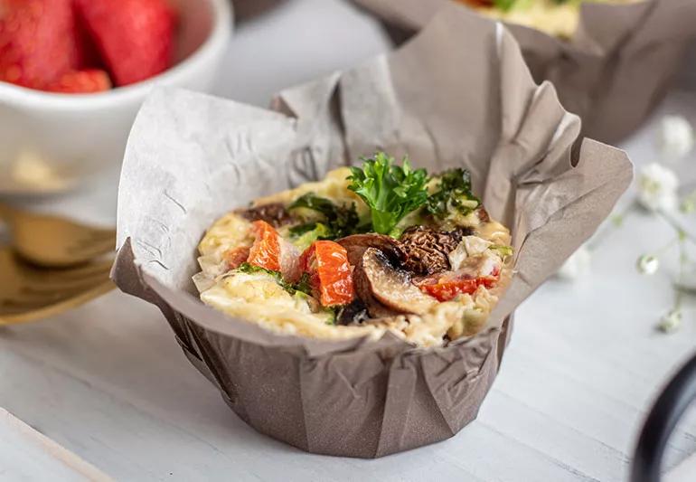 Small individual omelet in a muffin-sized ramekin, topped with tomatoes, greens and mushrooms