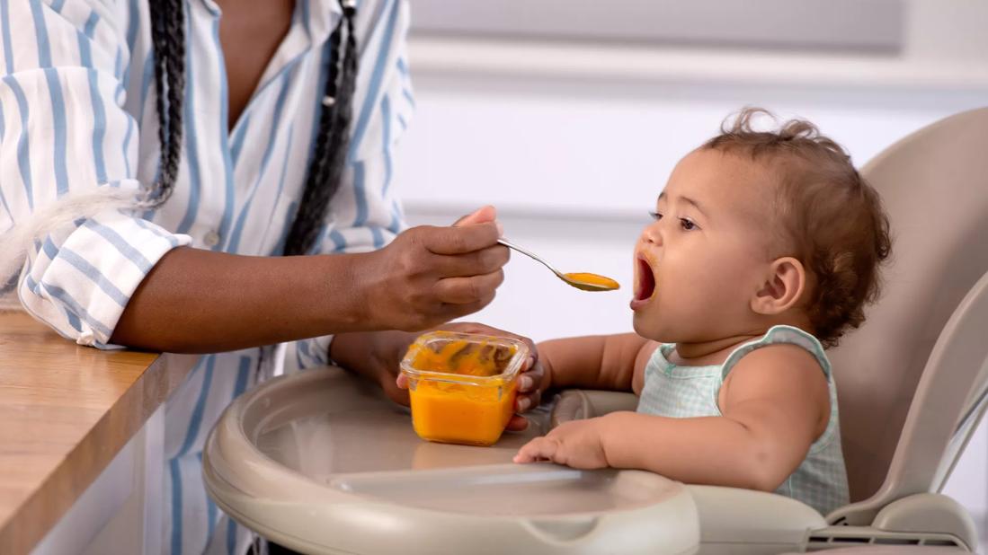 Caregiver feeding baby food to child in highchair