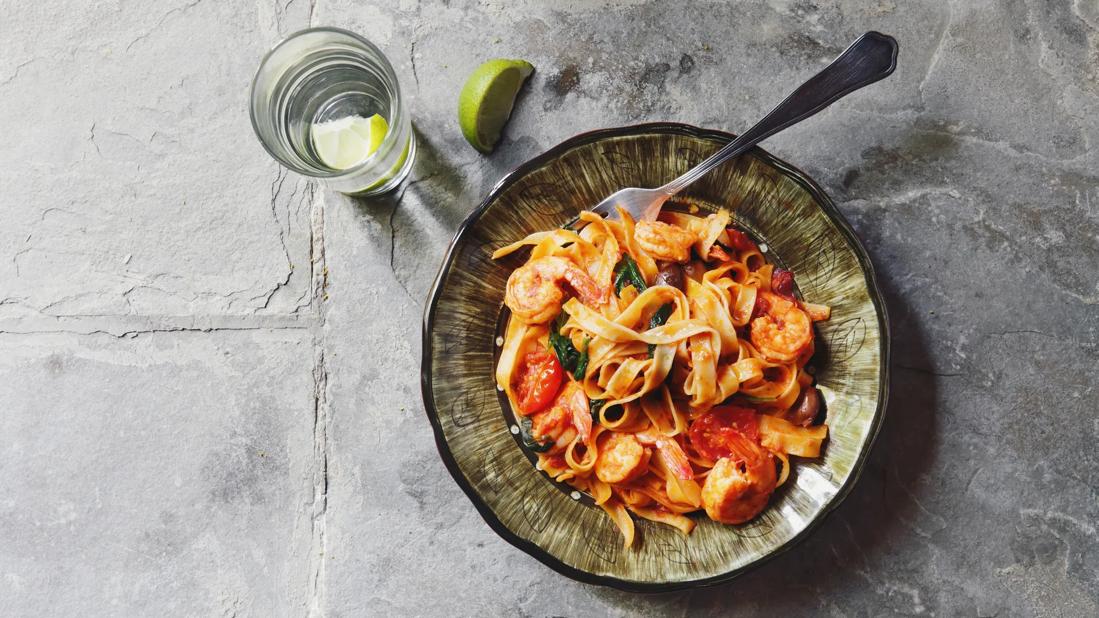 Italian pasta with shrimp in bowl with fork, glass of lime water next to, on stone table