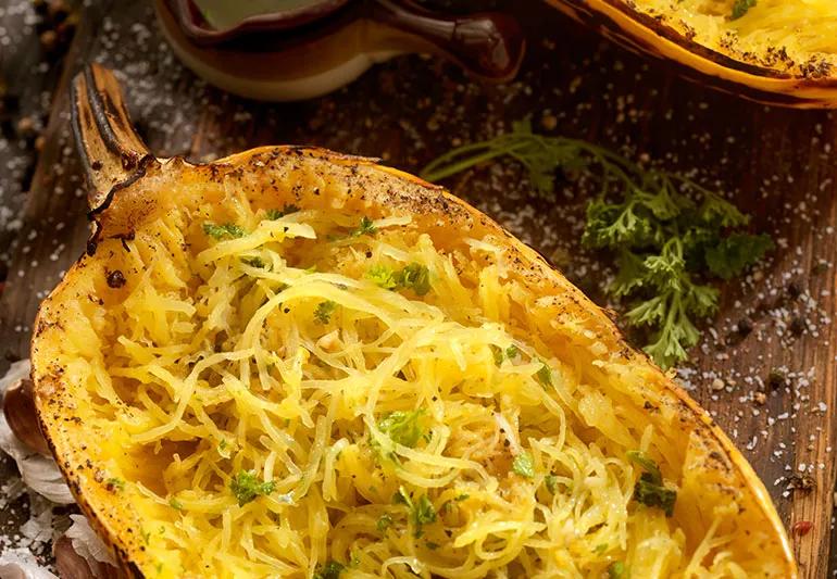 Spaghetti squash with green herbs in a hollowed-out half of a gourd atop a kitchen counter
