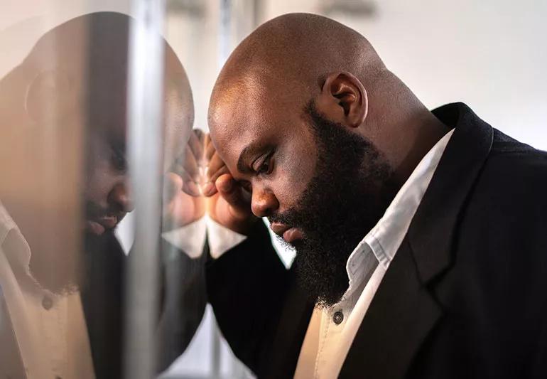 Bearded man leaning on reflective wall.