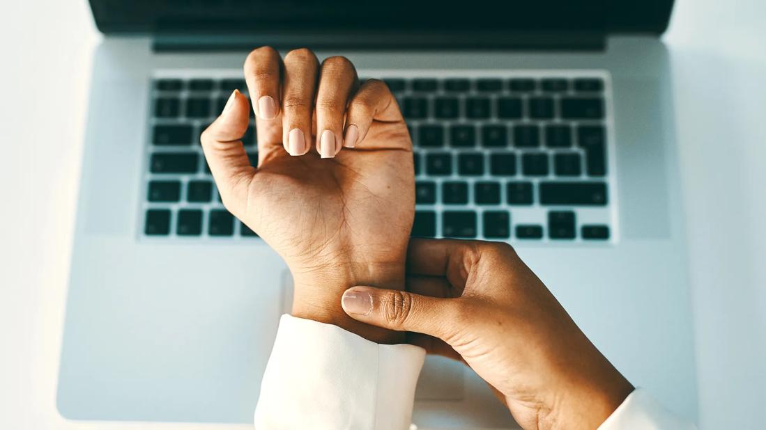 Hand applying pressure to wrist on other hand, hovering above keyboard