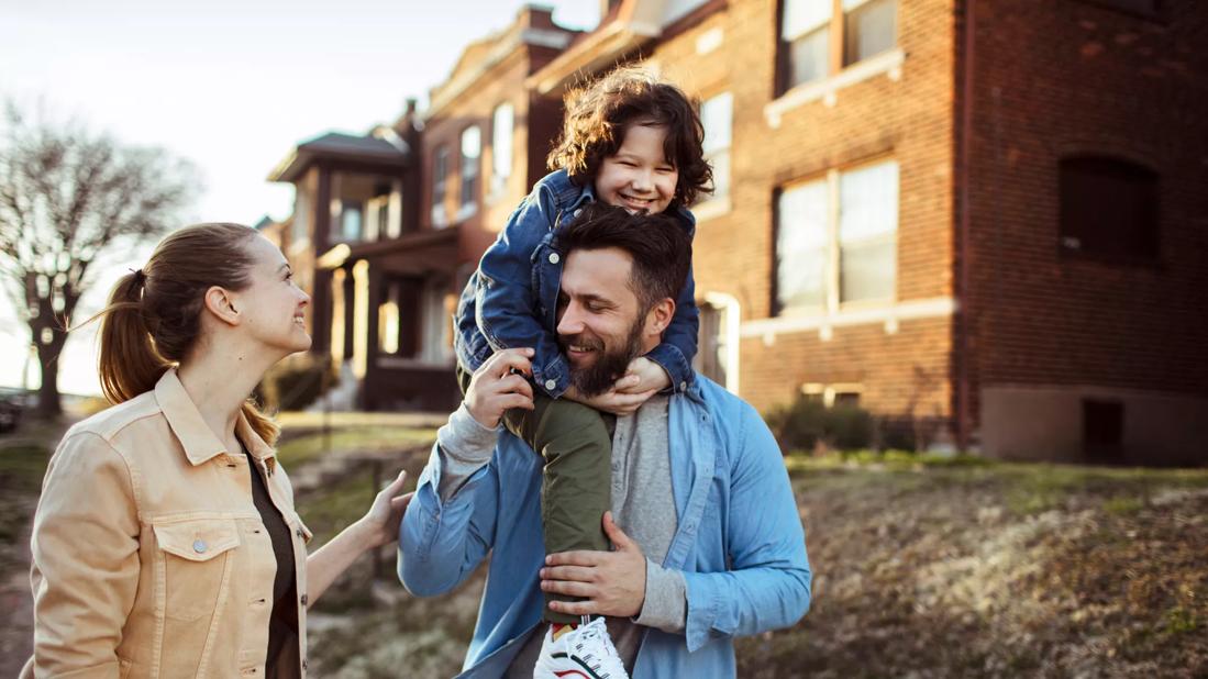 Two caregivers, with one holding a child on shoulders, walking happily outside