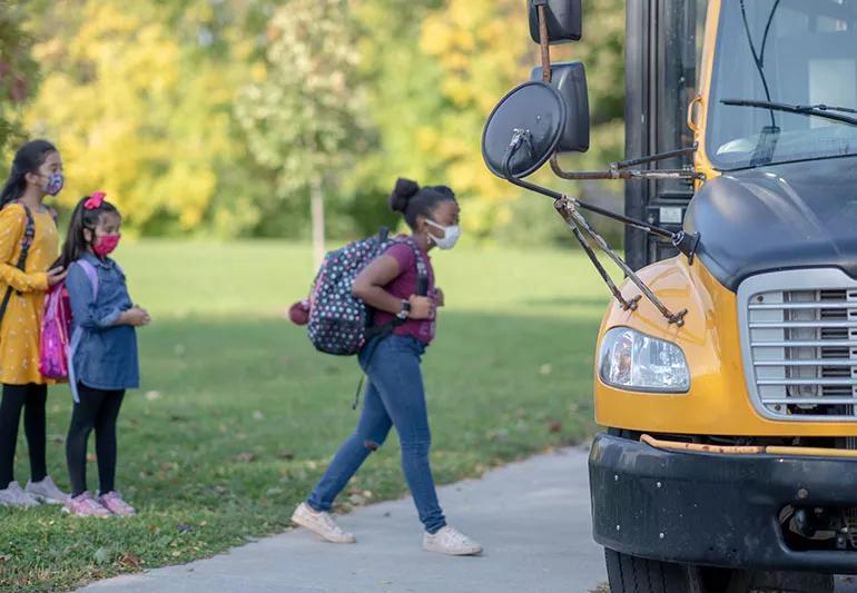 School-aged child wearing a mask while walking up to a school bus