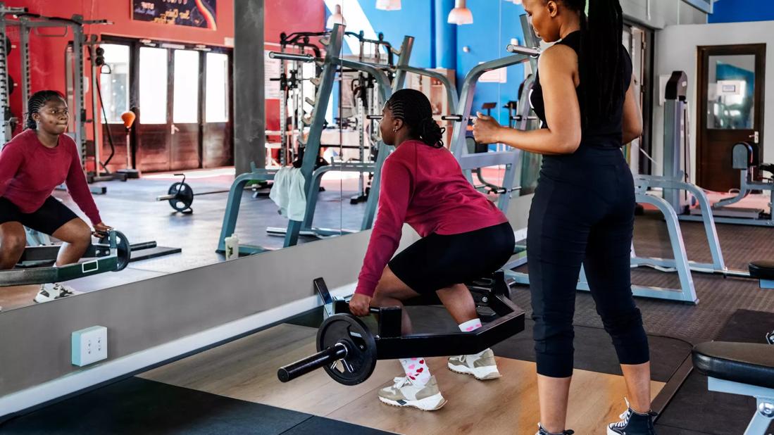 person lifting weights in a gym with a spotter behind them