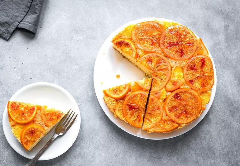 An overhead view of an orange upside-down cake with a single slice set aside on a small plate