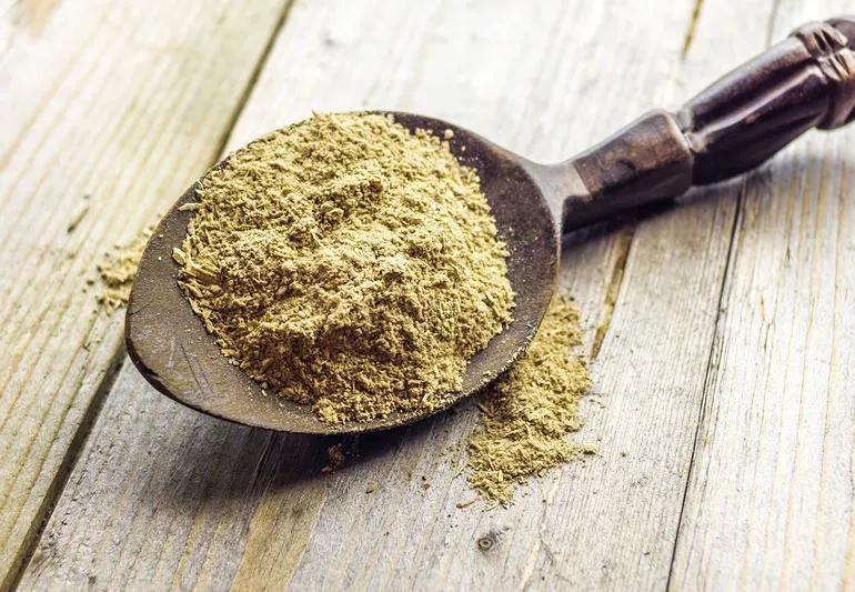 Kava powder loaded onto a dark wooden spoon resting on a wooden table.