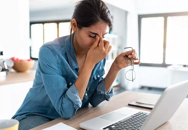A person sitting at a laptop pinching the bridge of their nose like they are tired