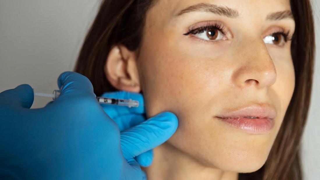 Gloved hands administering an injection into the jaw of a person