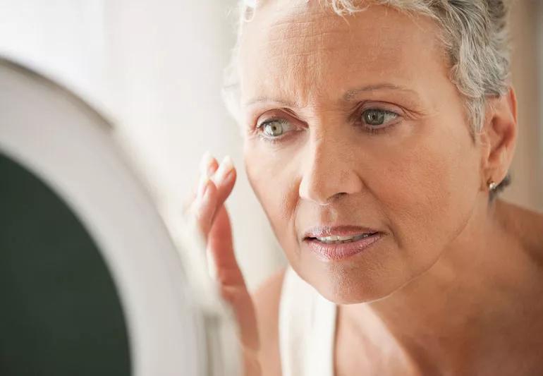 older female applying cream to face looking in mirror