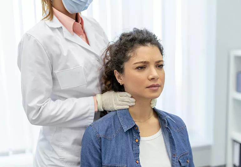 A healthcare provider examines someone's lymph nodes by placing their hands on a patient's neck.