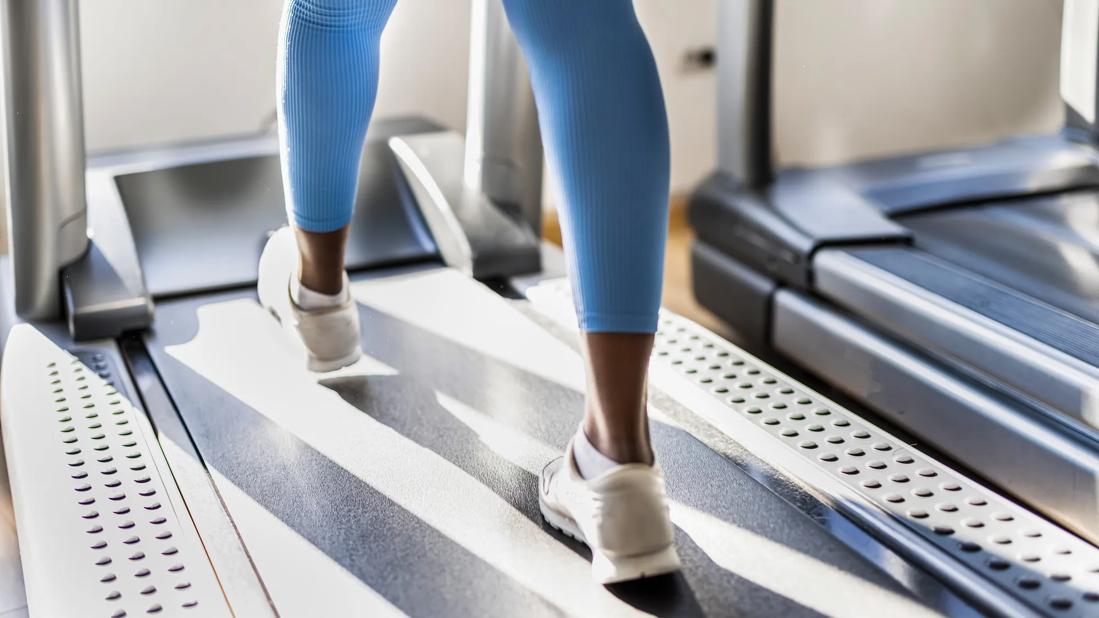 Legs and feet of person in blue leggings walking on a treadmill at gym