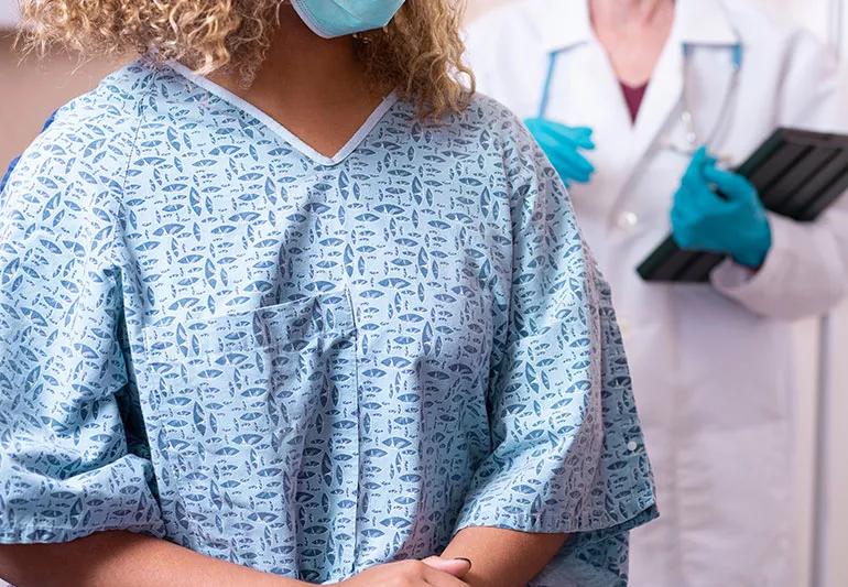 Person in a patterned hospital gown with doctor over their shoulder