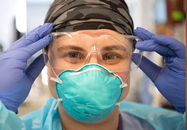 A healthcare provider wearing a camouflage head covering, a face mask and goggles.