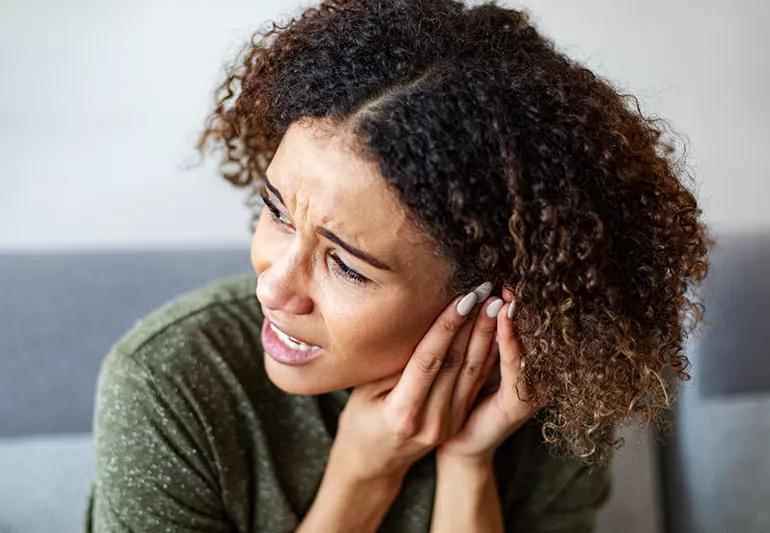 A woman cupping her left ear with both hands, with a look of pain on her face