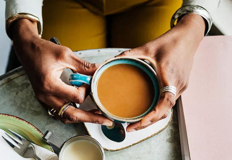 Top view of a person holding acoffee cup over a table at breakfast.