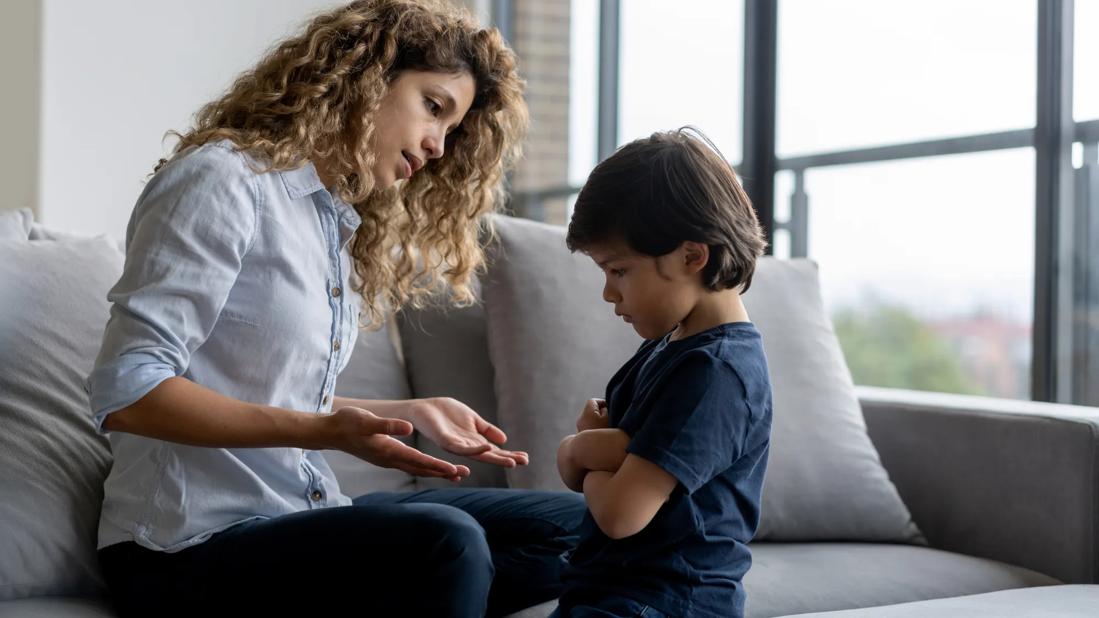 Caregiver talking to pouting, upset child with arms crossed