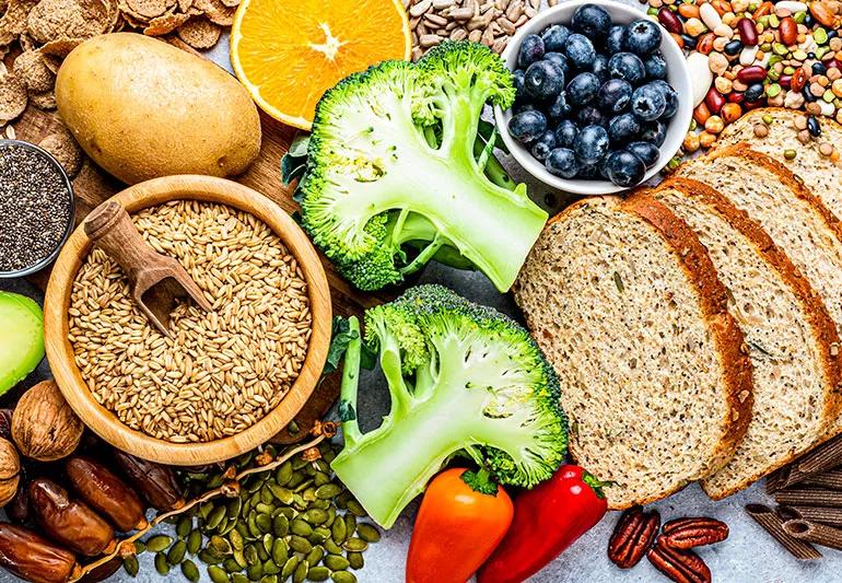 Different kinds of high fiber foods including broccoli, seeds and nuts, wheat breads and other vegetables.