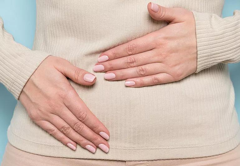 A close-up of a pair of hands wearing pink nail polish holding their torso