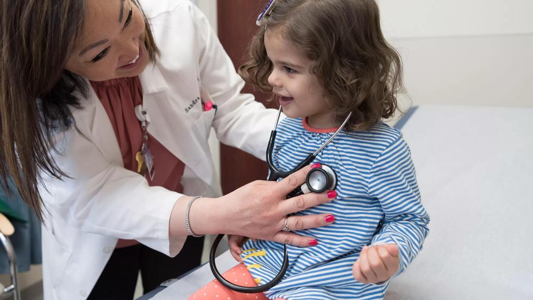 Physician smiles with child while using stethoscope