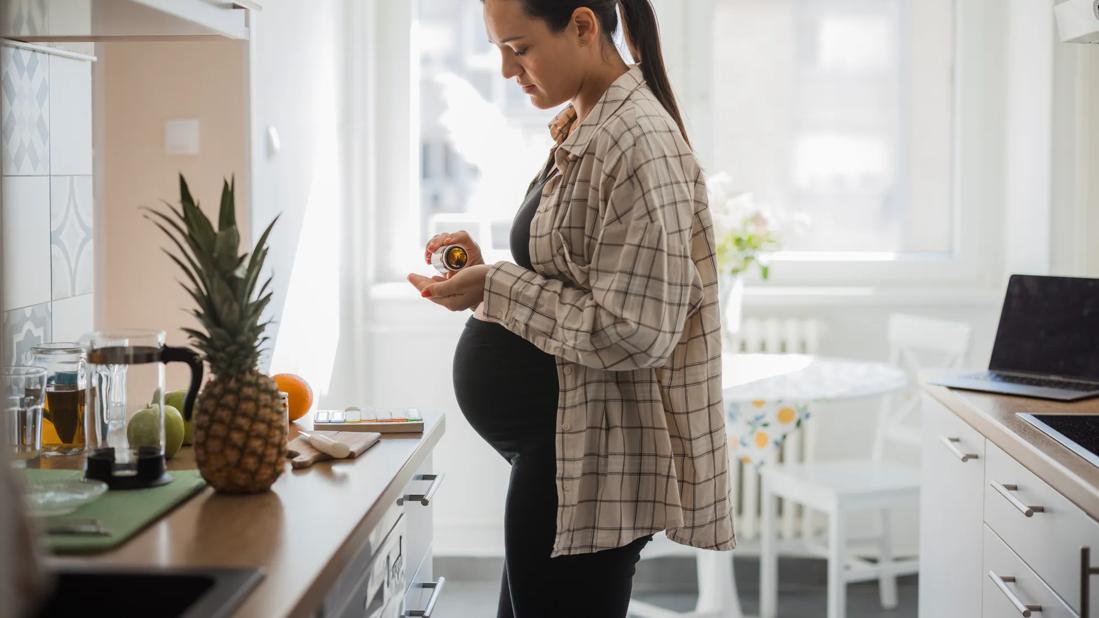 Pregnant woman standing in kitchen, pouring medication into hand