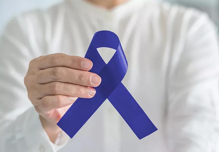 A person holds up a blue ribbon that represents Huntington's Disease awaraness.