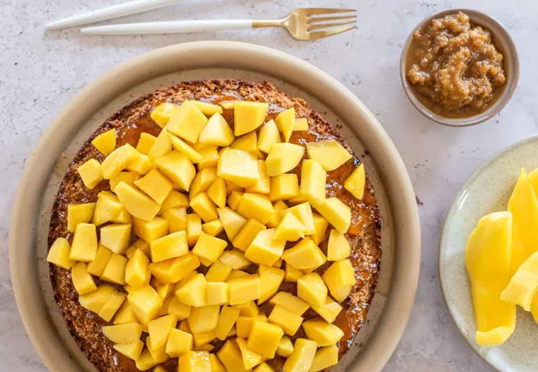 Brown cake topped with fresh mango chunks next to a plate of mango and a fork