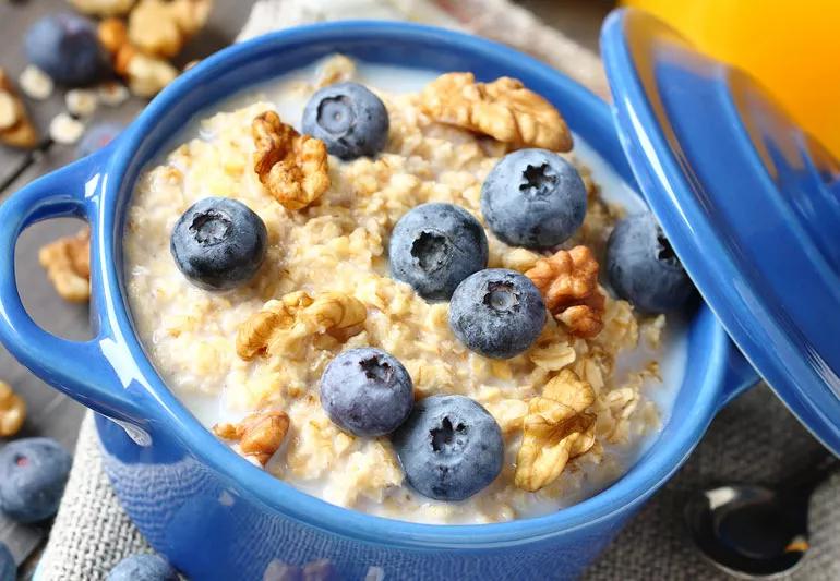 A blue bowl of oatmeal in milk with walnuts and blueberries