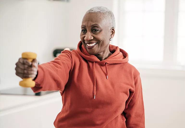 An elderly person is smiling while lifting a small 5-pound dumbbell.