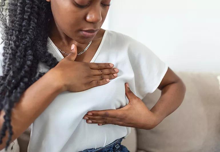 Adult in white blouse squeezes top and bottom of left breast as if to check for lumps