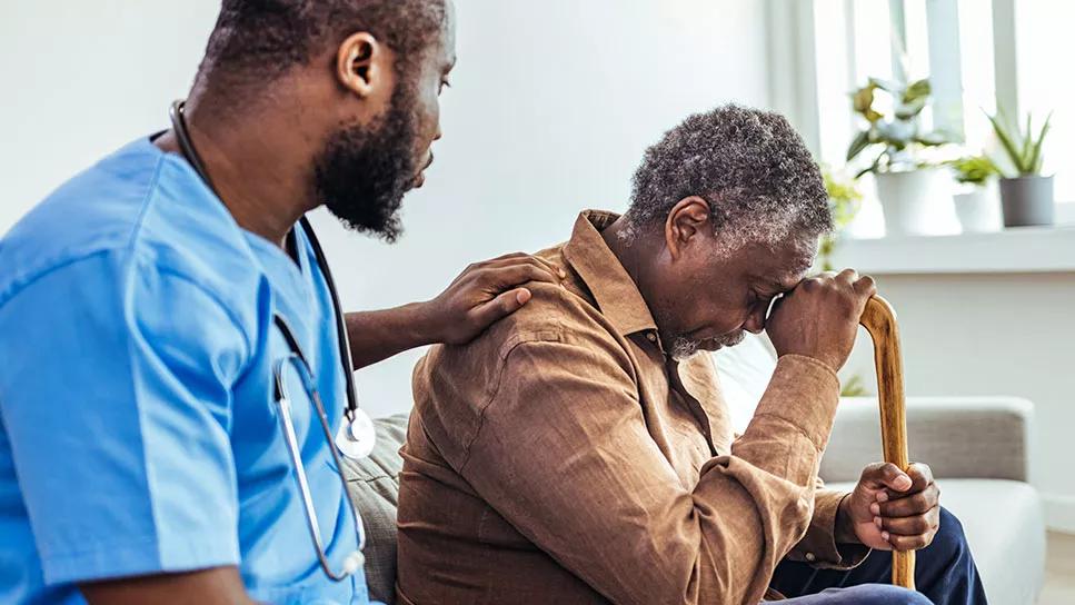 Caregiver and elderly male with head bent down