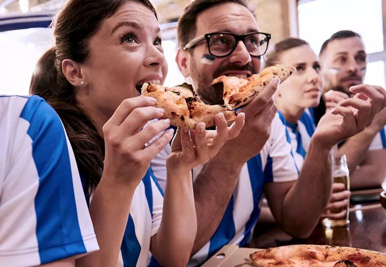 Stressed fans eat pizza while watching game.