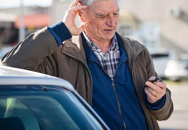 Elderly person in parking lot holding car keys and looking confused.