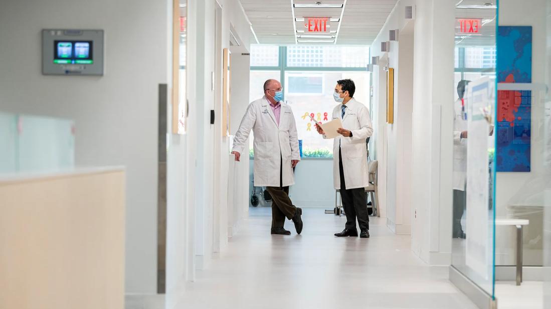 Two physicians standing at the end of the hallway talking