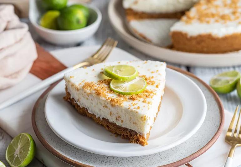 A piece of key lime pie, topped with thin slices of lime, sits on a small white plate.