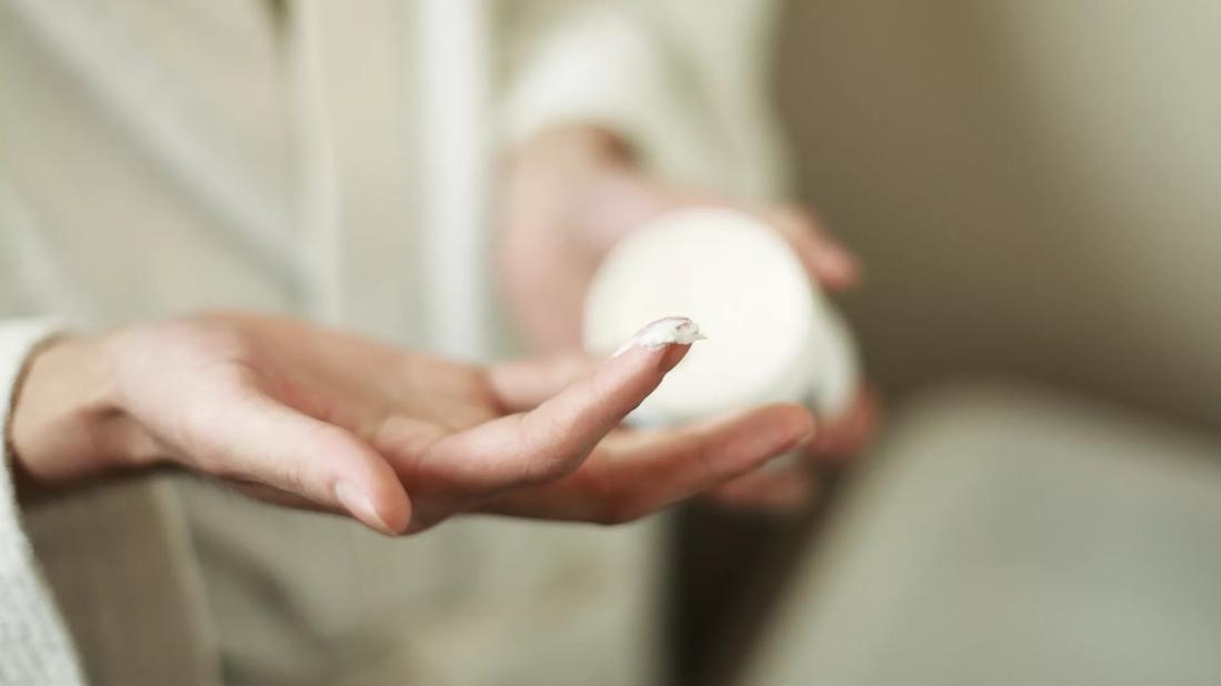 Person holding jar of moisturizer, with moisturizer on fingers