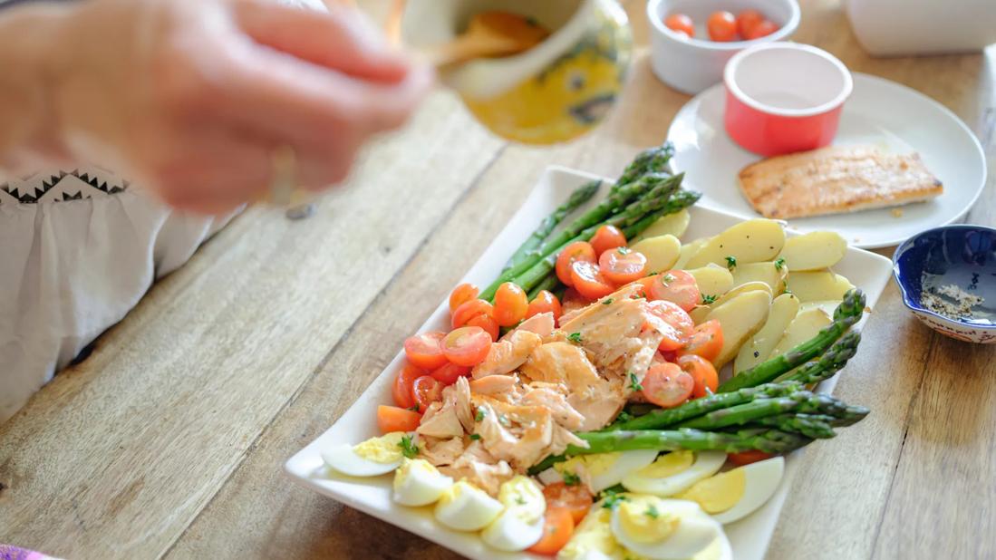 Person preparing healthy fish platter with veggies in kitchen