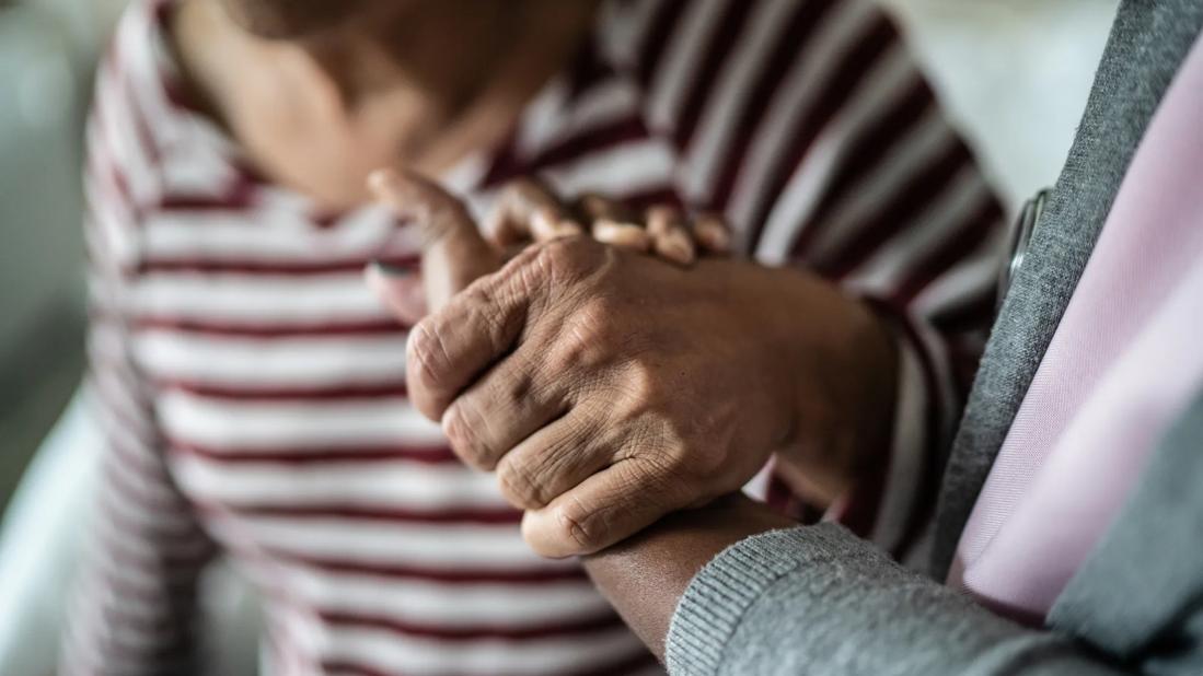 Elderly patient’s hand being held by a caregiver