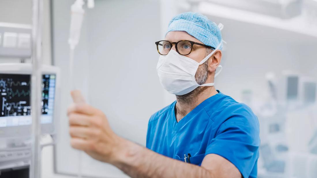 Healthcare provider in scrubs and mask in operating room checking IV line