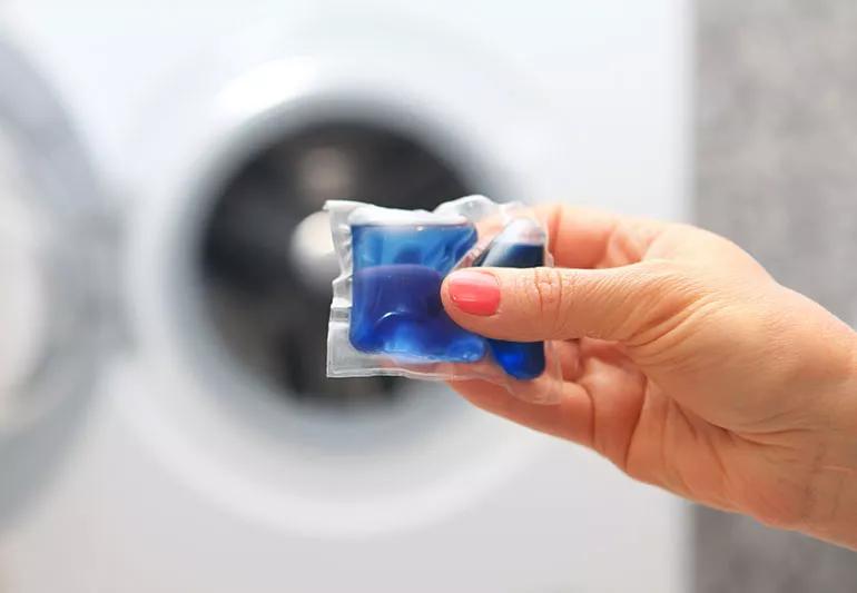 Closeup of a hand holding a laundry detergent pod with washer open in the background
