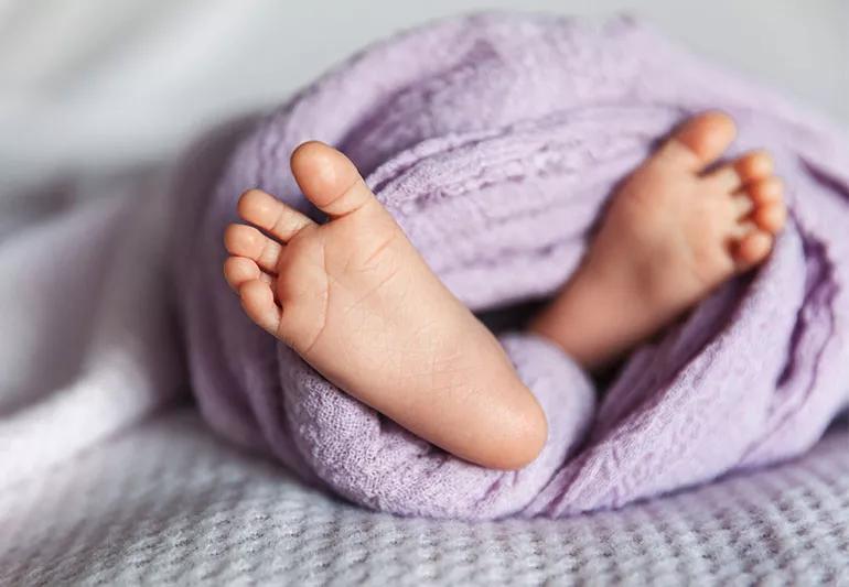 A photo of very tiny baby feet sticking out of a lavender blanket