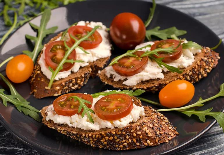 Roasted tomato, cheese and arugula toasts on a black plate