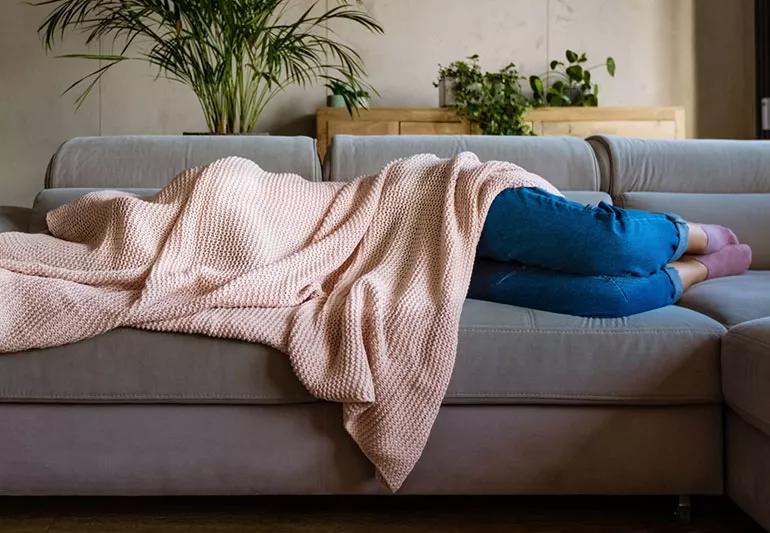 Person with migraine headache sleeping under blanket.