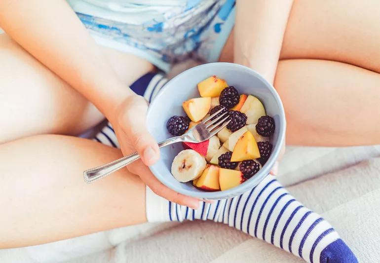 Woman eating bowl of mixed fruits for snack