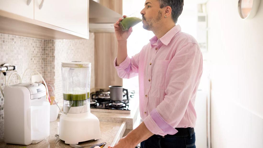 Person drinking smoothie in kitchen, with blender on counter