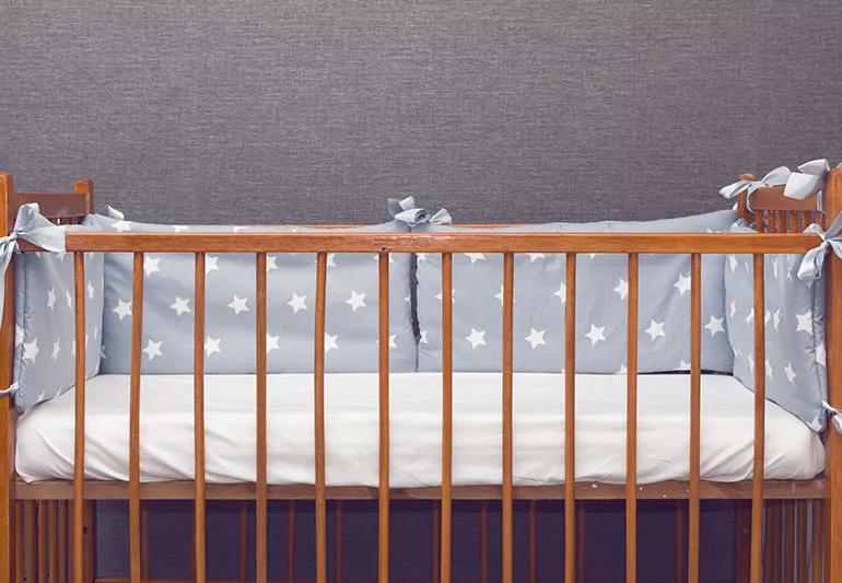 A photo of a wooden crib with star patterned pillows and white sheets