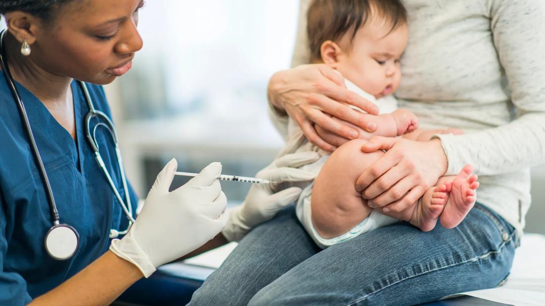 Caregiver holding a baby receiving a vaccination shot from a healthcare provider