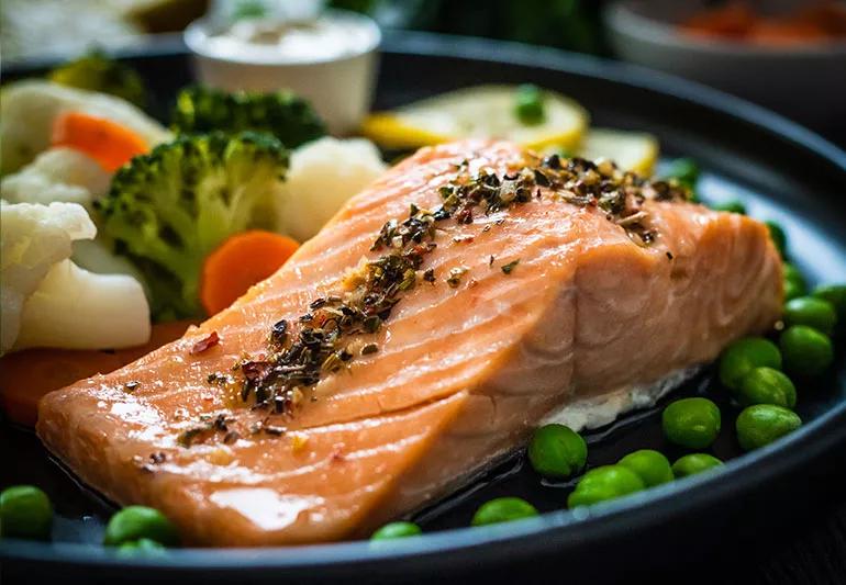 Salmon filet covered in herbs on a plate with broccoli and peas